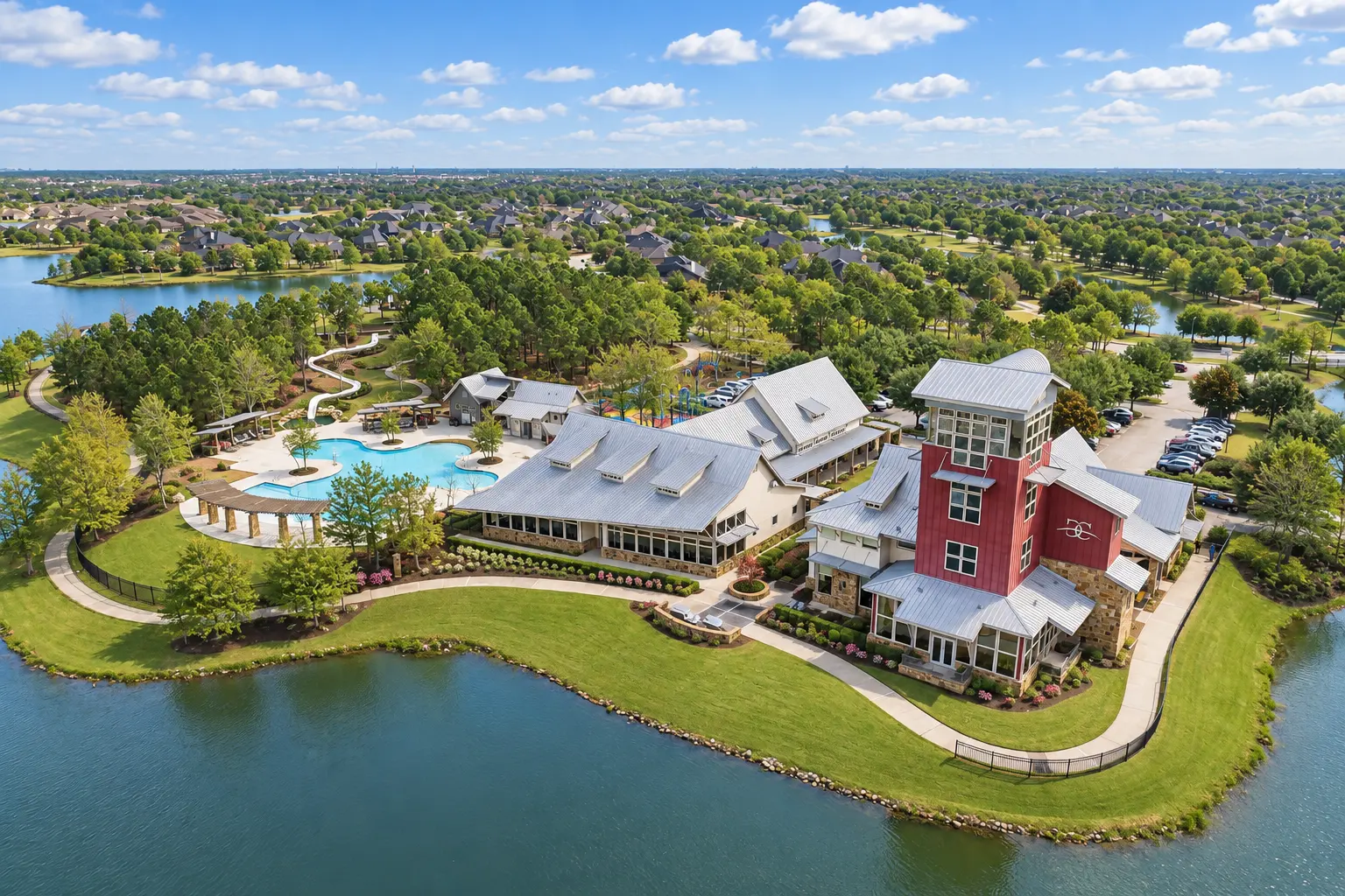 Aerial view of a lakeside community amenity center with a pool, water slide, and clubhouse in Fulshear, Texas
